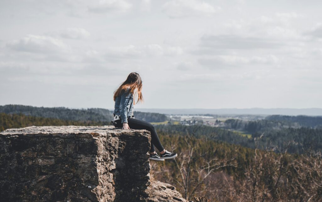 A young woman sitting on a cliff looking out over the forest below