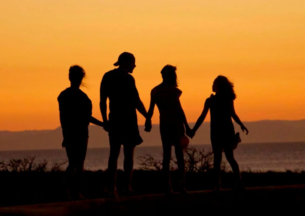 A family silhouetted in the sunset holding hands and looking out to the ocean.