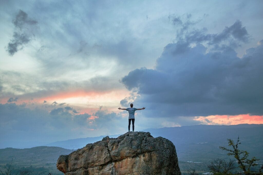 person standing on a rock facing a sunrise