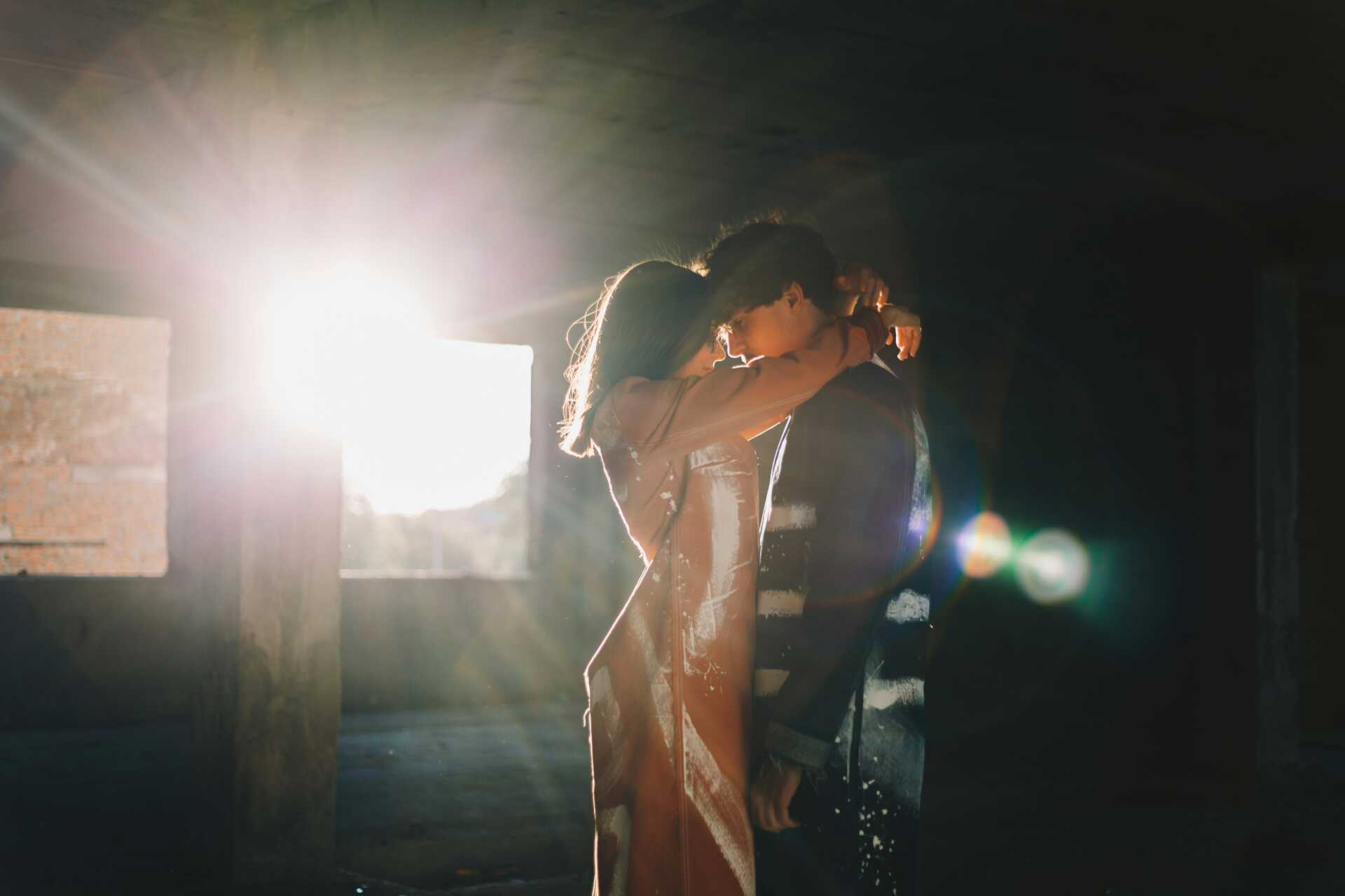 a couple embracing with a flare of sunlight shining through the door behind them