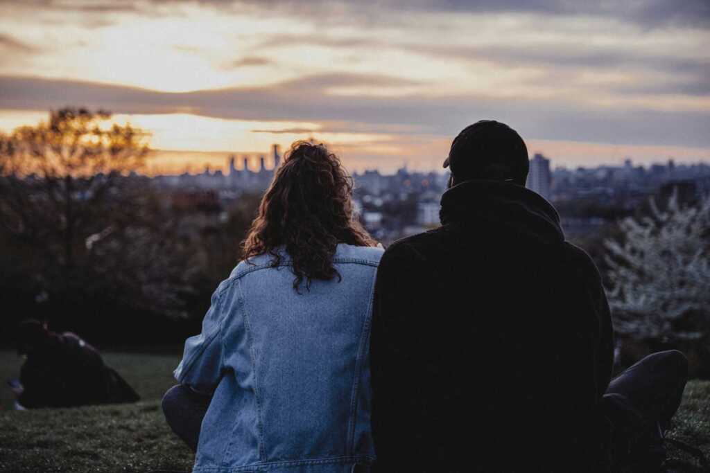 A couple sitting on a hill looking towards a city skyline in the distance