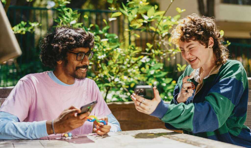 Two people sitting at a table outside looking at a phone and smiling