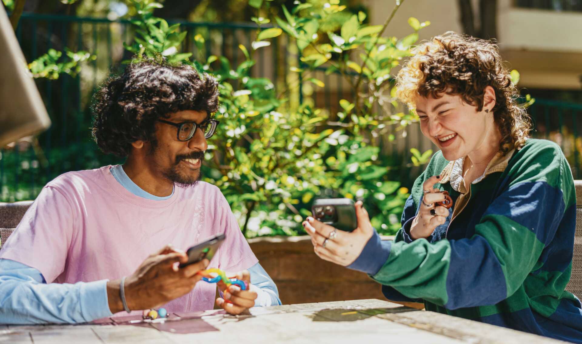 Two people sitting at a table outside looking at a phone and smiling
