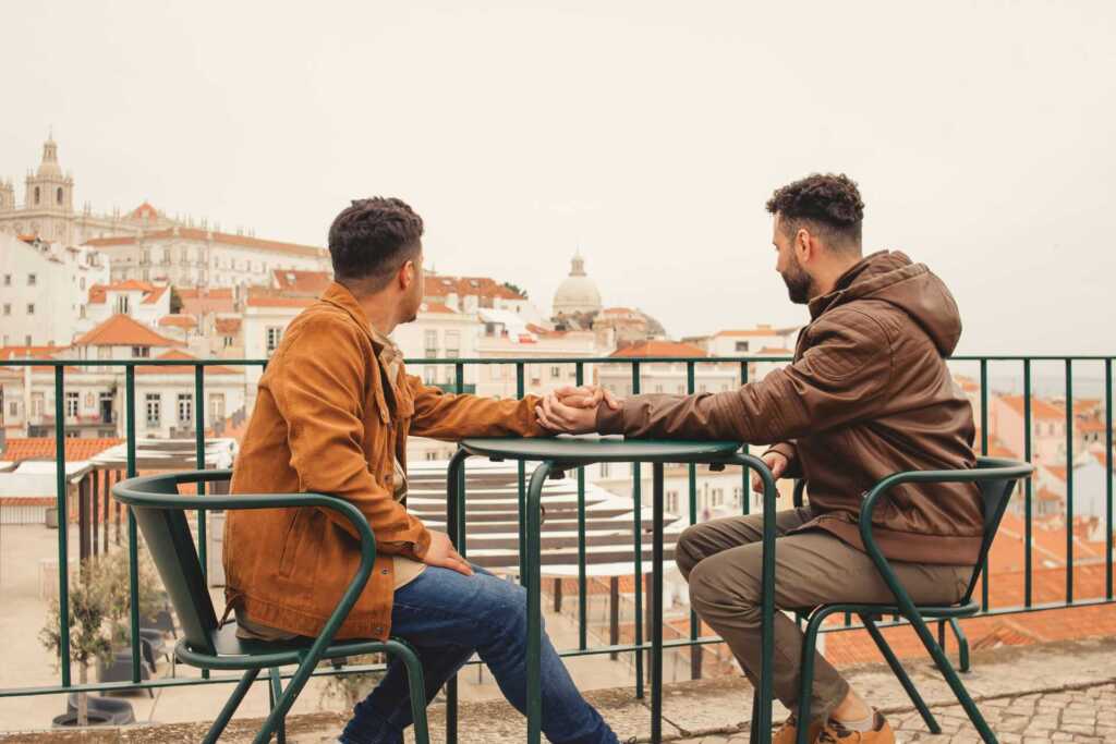two men holding hands over a table outdoors looking out into the distance