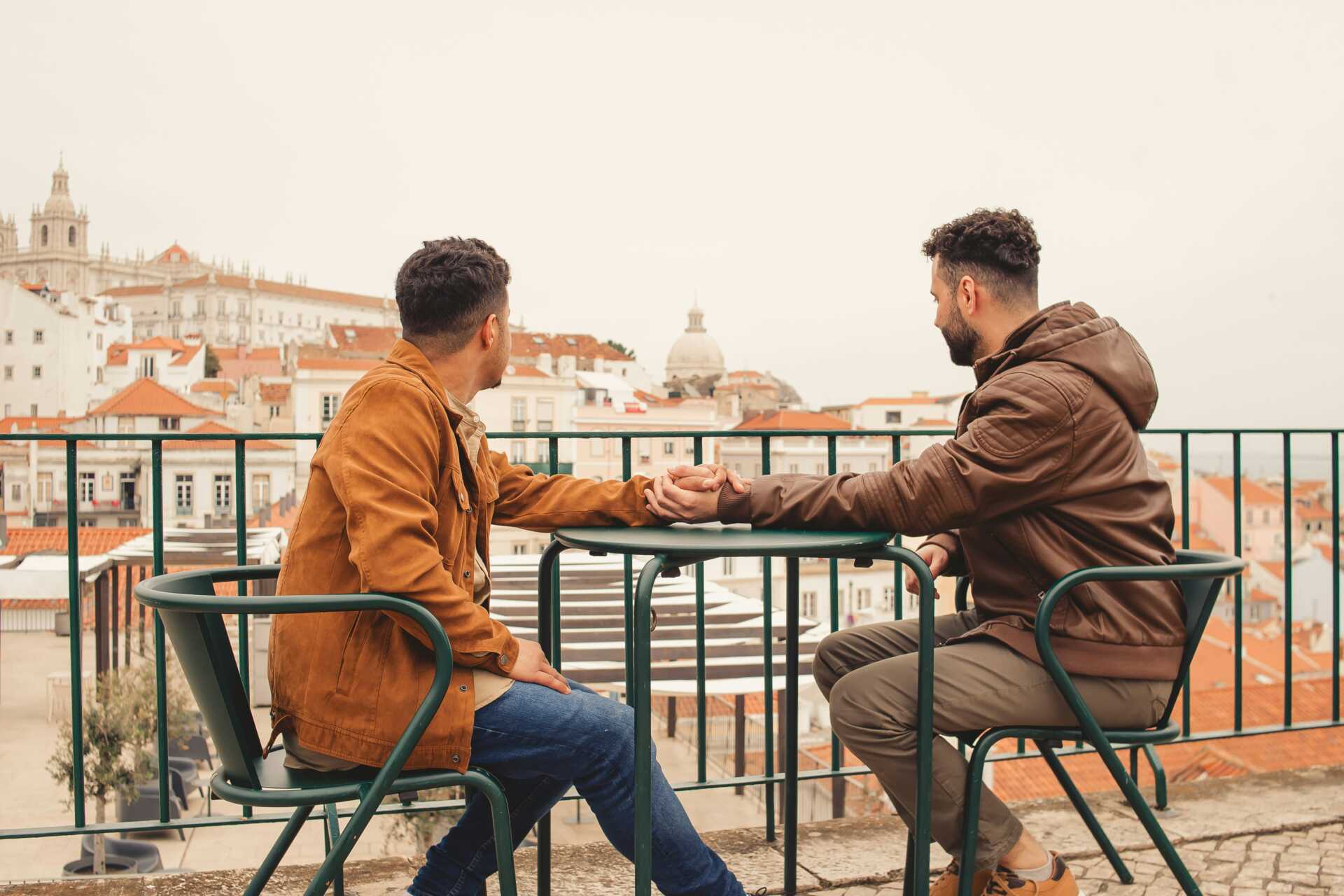 leticia fracalossi aGA6pBx71 0 unsplash two men holding hands over a table outdoors looking out into the distance