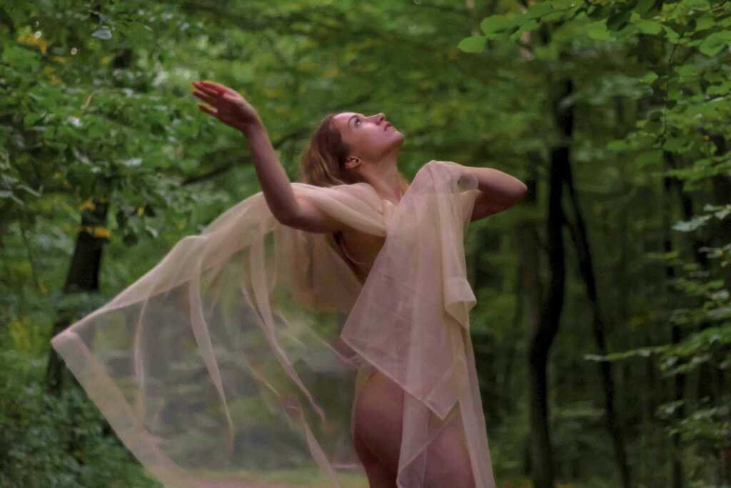 A woman in the forest draped in tulle fabric and looking up to the sky