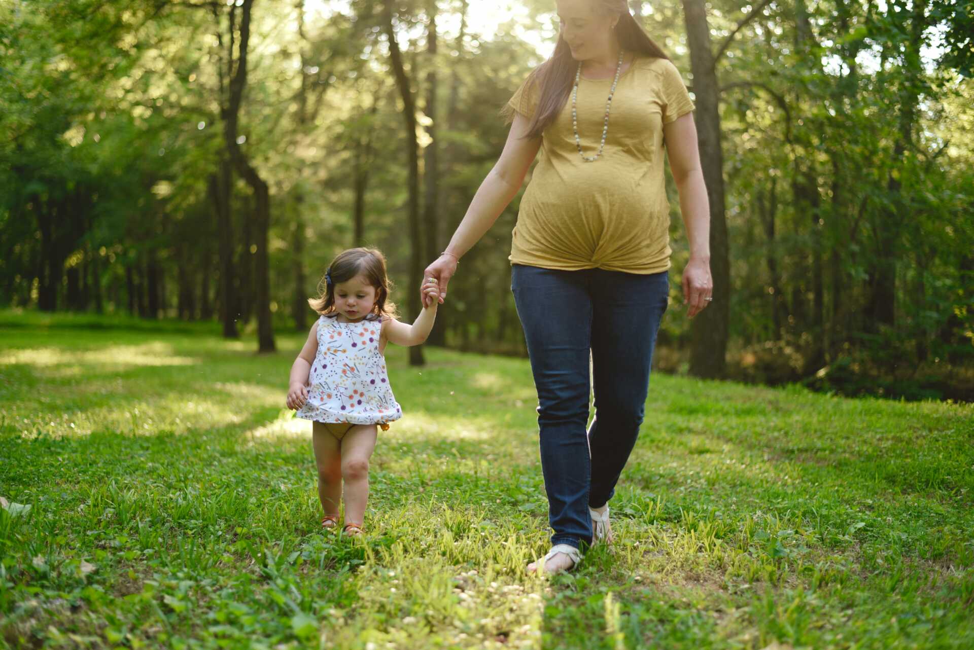 christian bowen vicc6MWQDcA unsplash A pregnant woman walking hand in hand with her young child through a grassy field