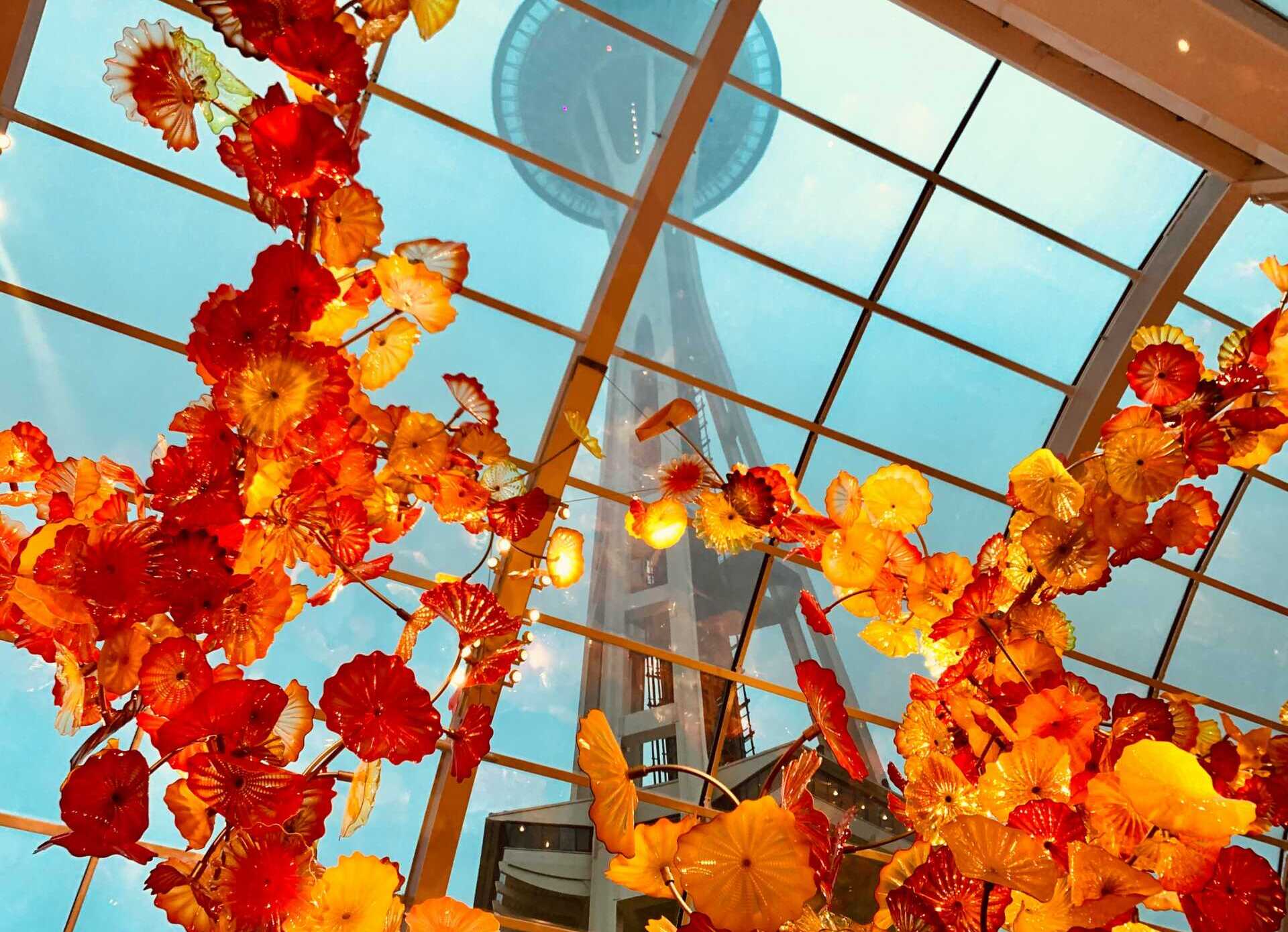 xh s yekOnsm1rE unsplash A view from the ground looking up at orange glass sculptures and a glass ceiling with the Space Needle towering above
