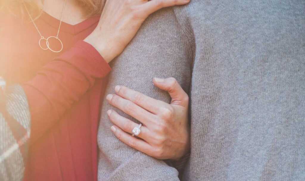 An engagement photo with a women's arms wrapped around a man's showing off her engagement ring