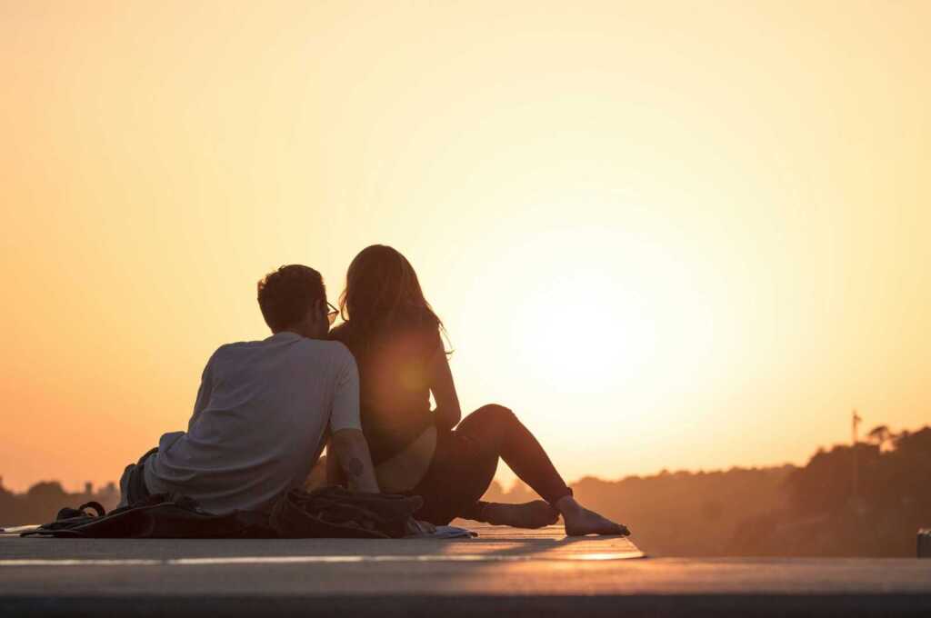A couple leaning against each other looking at the sunset