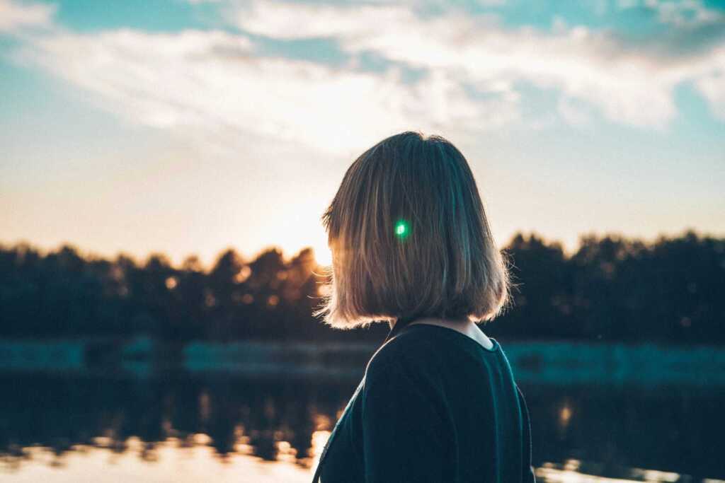 A woman looking out at the sunset near a beautiful lake