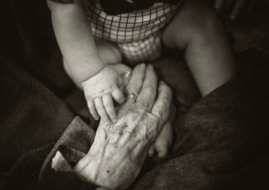 a black and white photo of a baby sitting across from a grandparent