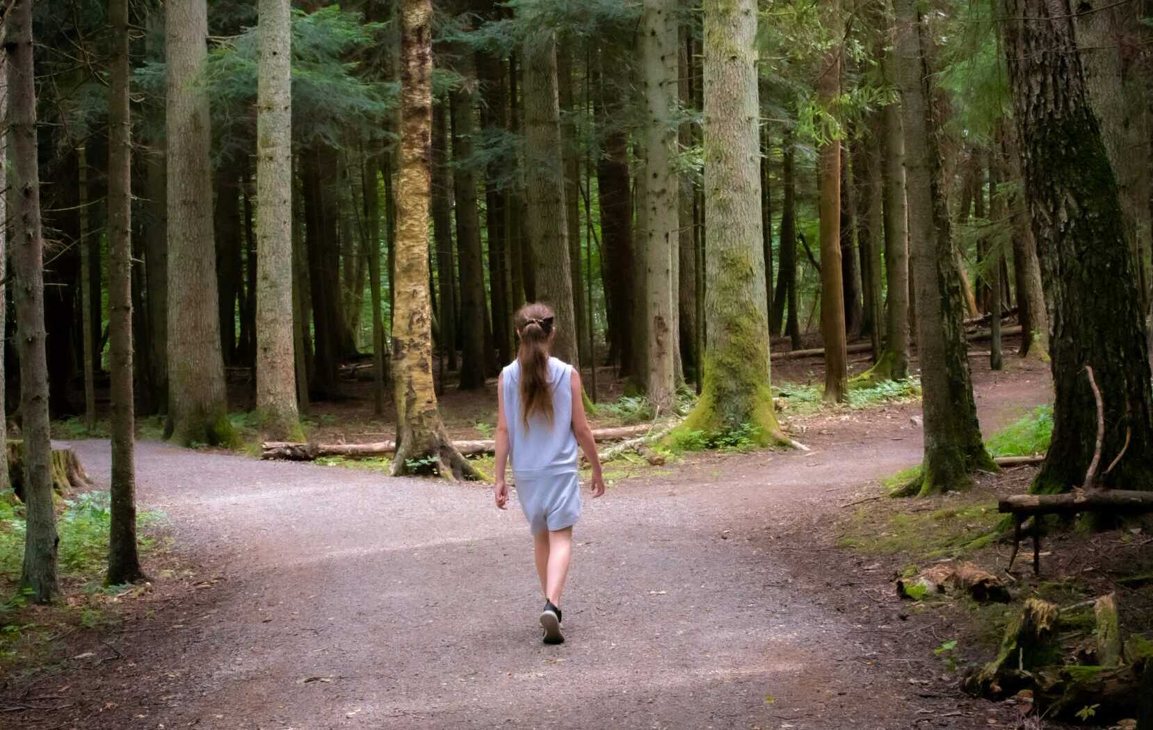 einar storsul K3W7I7x37Xk unsplash A woman walking towards a crossroad in the forest