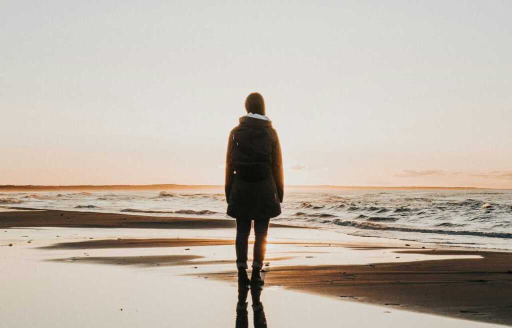 A woman on the beach in a coat looking out to the ocean