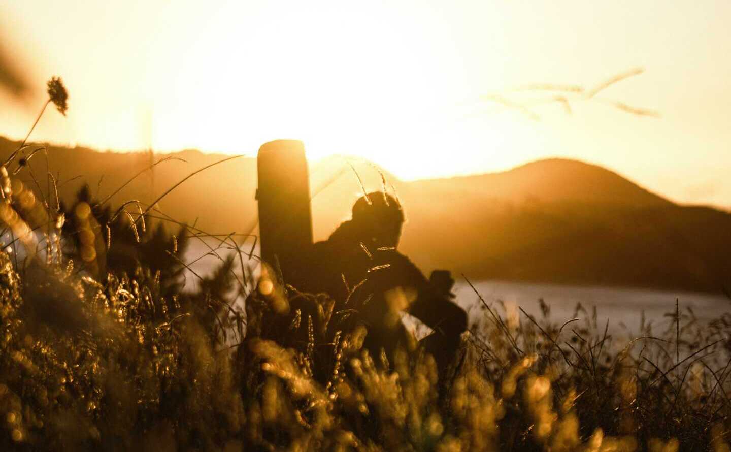 A man sitting in a field looking out to the hills during a sunrise
