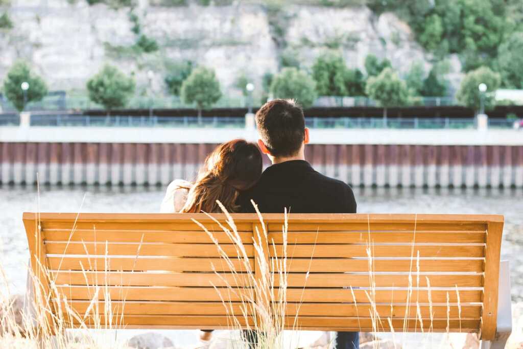 A view of a couple sitting on a bench from behind