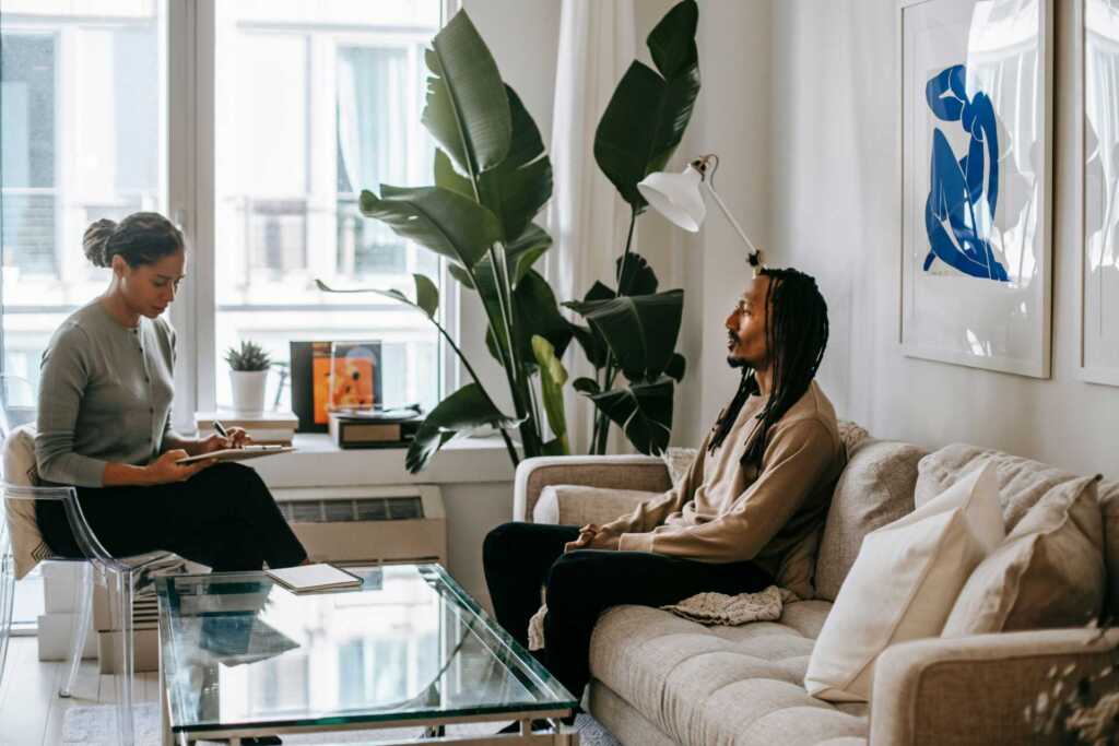 A serene therapy session between therapist and client in a cozy, light-filled living room.