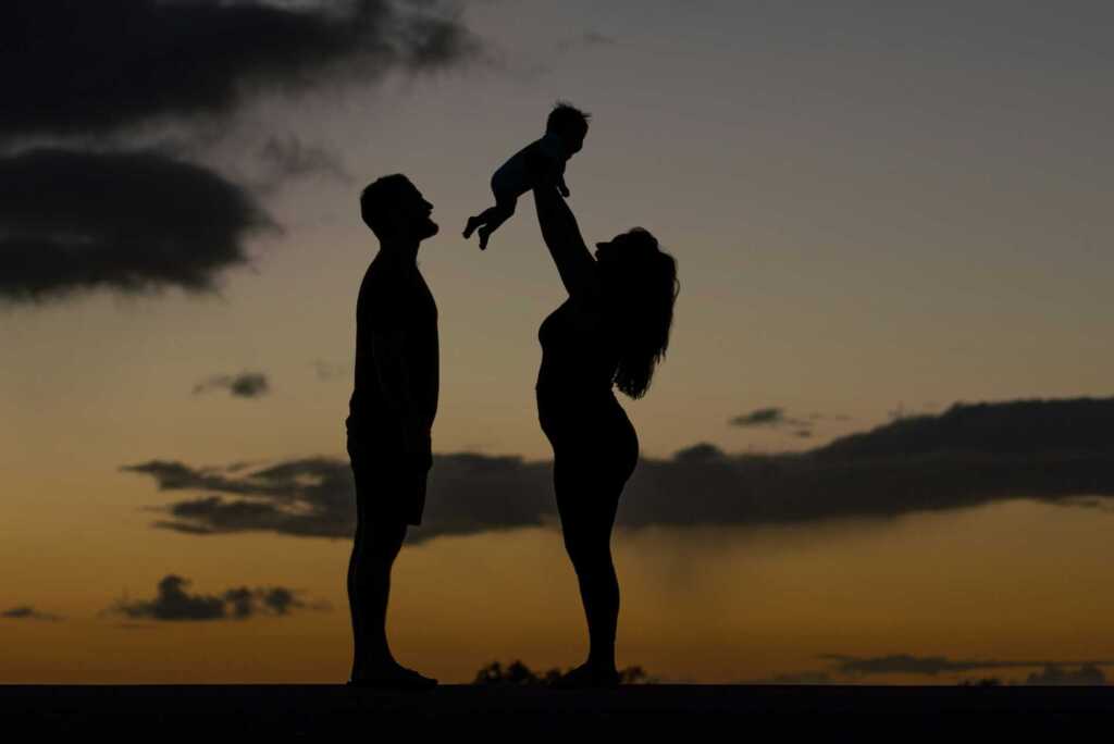 A couple silhouetted in the sunset holding up their baby