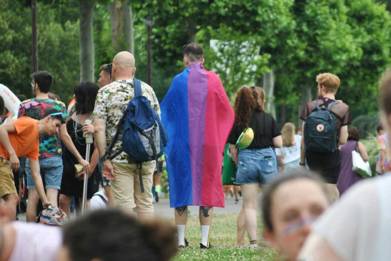 delia giandeini XYOlLlLLsOU unsplash A man with a bisexual pride flag draped over his shoulders and standing in a crowd of people
