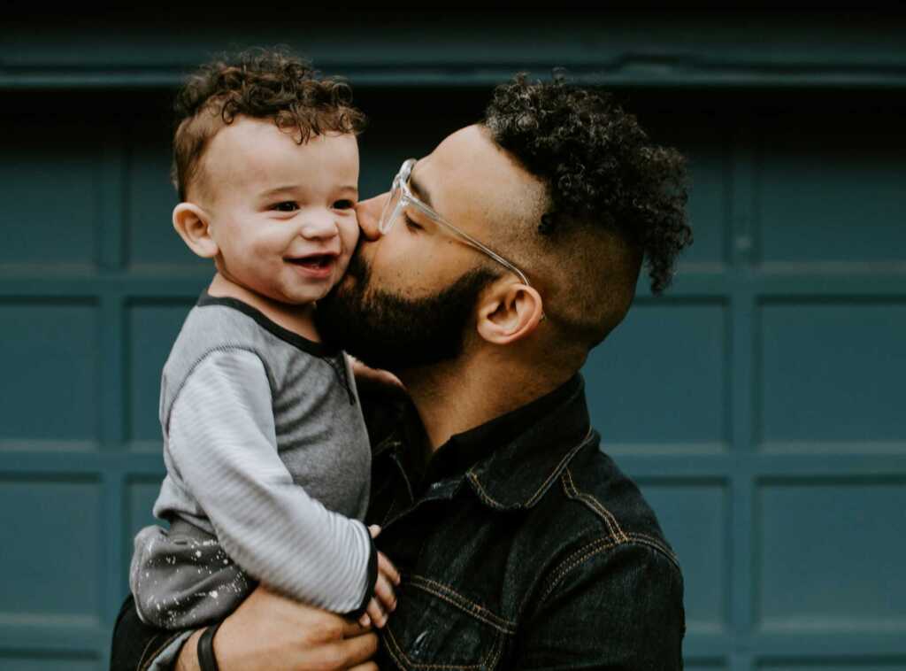a dad holding his baby and kissing him on the cheek