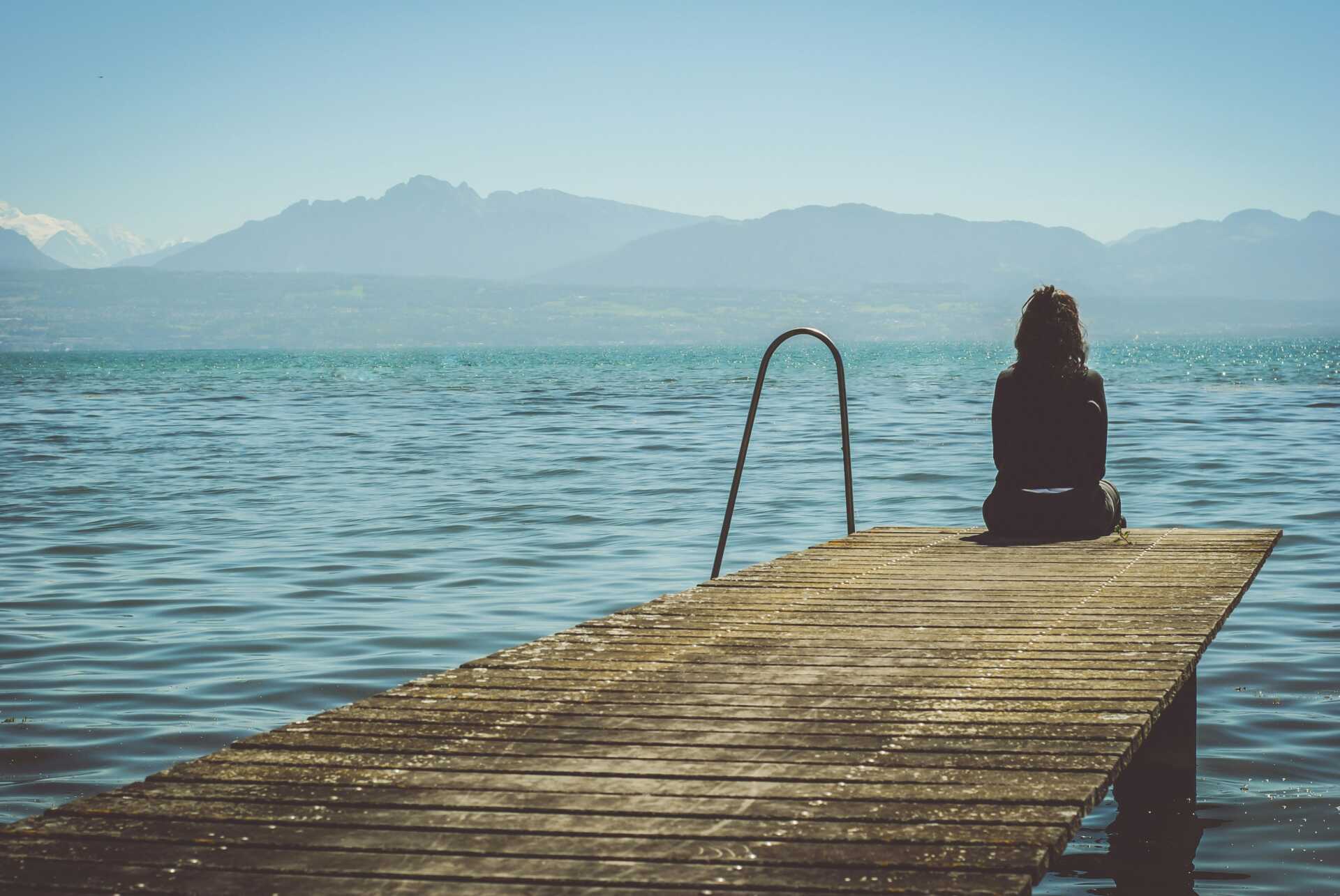 paola chaaya eAkjzXCU0p0 unsplash A woman sitting on a dock looking out over the water
