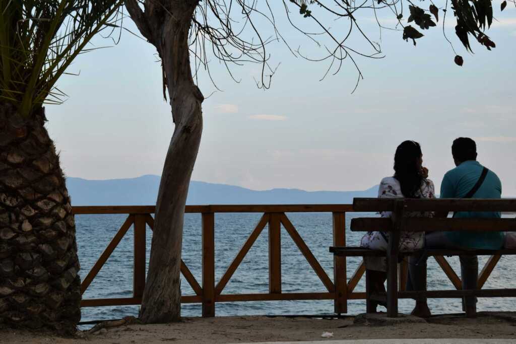 A couple sitting on a park bench looking out to the ocean